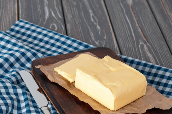 Wooden board with butter on blue checkered napkin, close up.