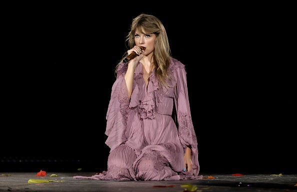 Taylor Swift kneels on stage while singing. 