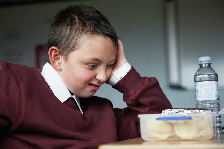 Schoolboy (8-10) sitting at desk staring at lunchbox, pulling face